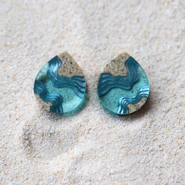 Light blue stud earrings on sand