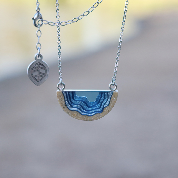 Dainty beach sand and blue resin necklace on beach